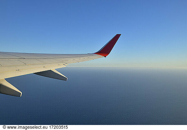 Wing of commercial airplane flying against clear blue sky