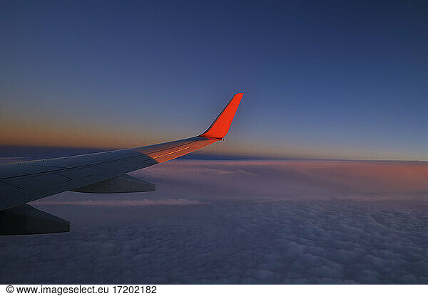 Wing of commercial airplane flying against sky at dusk