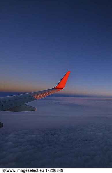 Wing of commercial airplane flying against sky at dusk