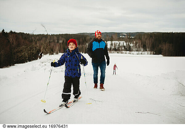 Winter fun boy smiling on skis with family behind him on snowy day