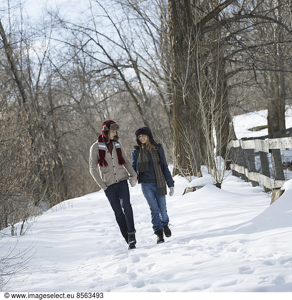 Winter scenery with snow on the ground. A couple walking hand in hand along a path.