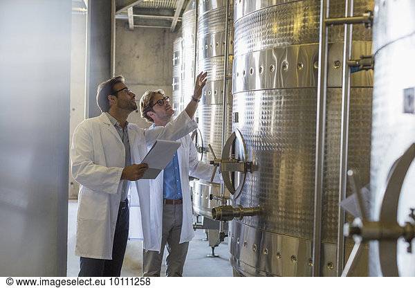 Winzer in Labormänteln prüfen Fässer im Weinkeller