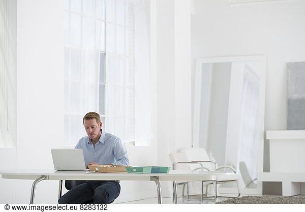 Wirtschaft. Ein Mann sitzt mit einem Laptop an einem Schreibtisch.