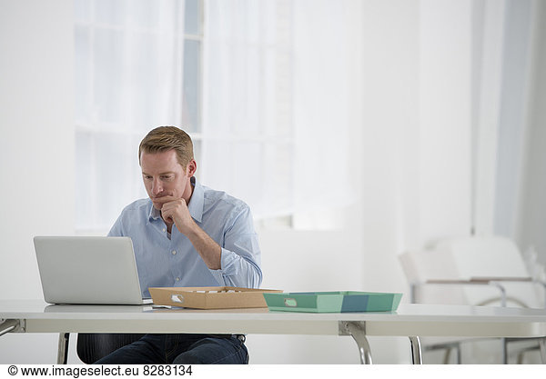 Wirtschaft. Ein Mann sitzt mit einem Laptop an einem Schreibtisch.