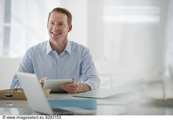 Wirtschaft. Eine luftige Büroumgebung. Ein sitzender Mann hält ein digitales Tablet.