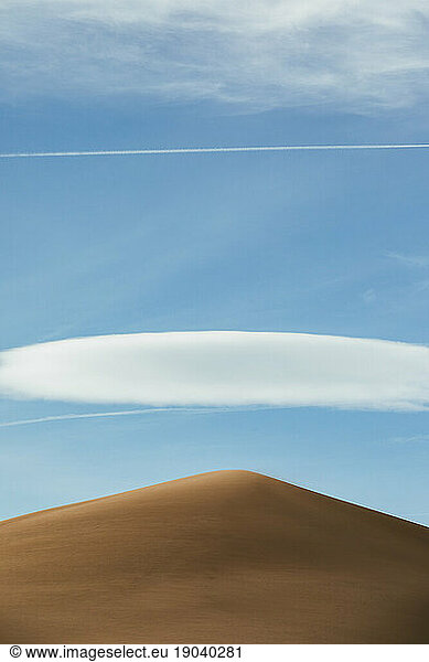 wispy clouds and chem trails frame a single golden sand dune