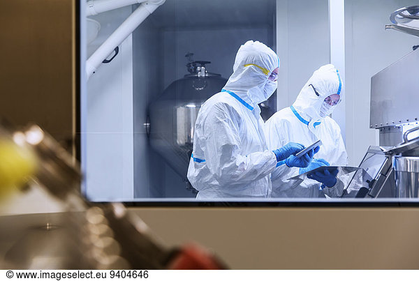 Wissenschaftler in sauberen Anzügen mit digitalen Tabletten im Laborversuch