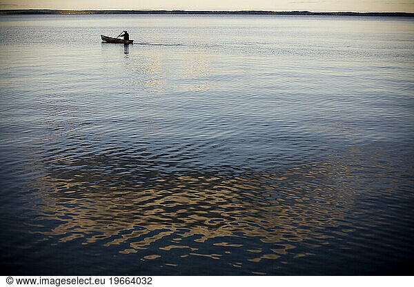 With a reflection of a cloud in the calm  blue water  a man drifts peacefully silhouetted against the smooth