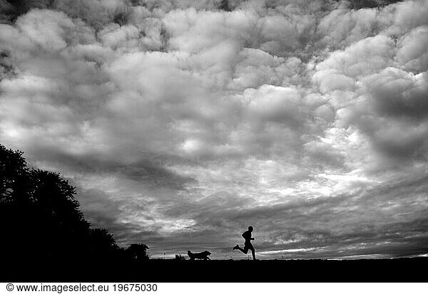 With amazing clouds covering the sky a man and his dog run across a grassy field near Corvallis Oregon.