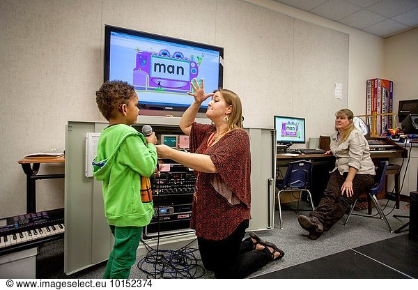 With signing a teacher uses a language video to teach a deaf child to speak into a microphone at the California School for the Deaf in Riverside. MODEL RELEASE.