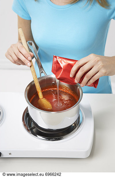Woman Adding Pectin to Red Pepper Sauce to Make Jelly