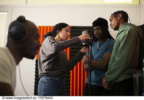 Woman adjusting microphone while rappers standing in studio