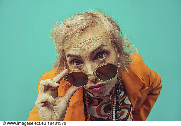 Woman adjusting sunglasses against colored background