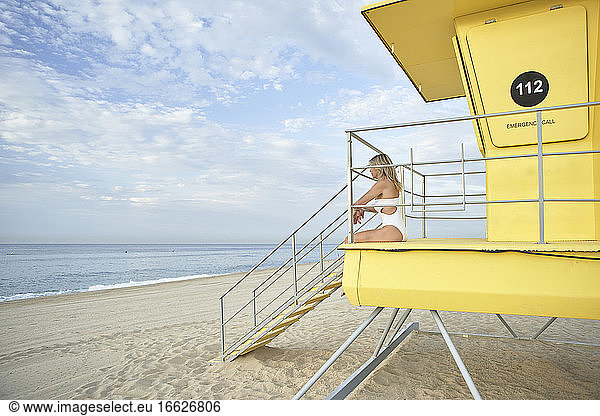 Woman admiring view while sitting at lifeguard hut on beach