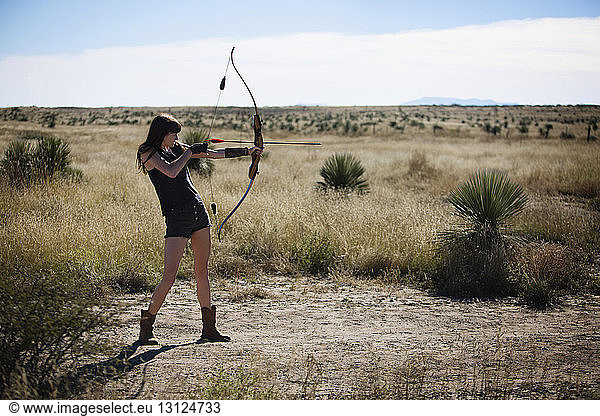Woman aiming with bow and arrow while standing on field