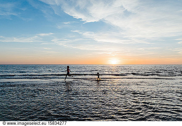 woman and child run in the shallow waters of a florida beach at sunset