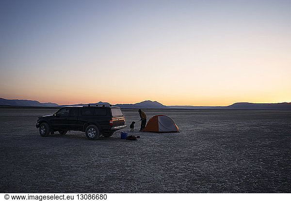 Woman and dog standing by car on field against sky at Alvord Desert