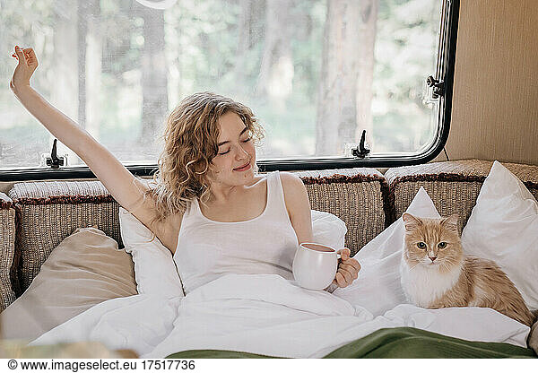 Woman and ginger cat in trailer with cup of coffee.