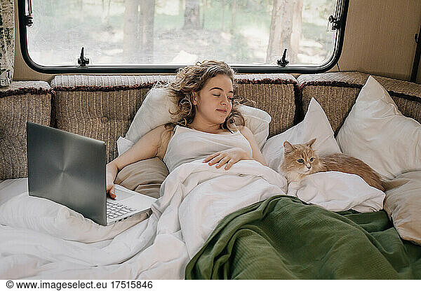 Woman and ginger cat in trailer with laptop.