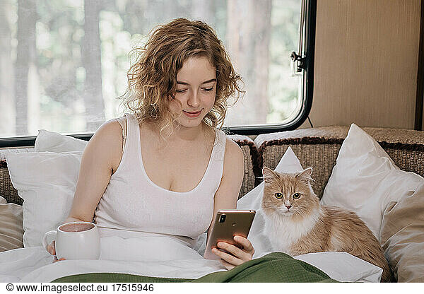 Woman and ginger red cat in trailer with phone.