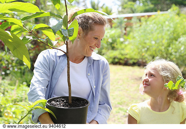 Woman and girl with tree seedling in sunny garden