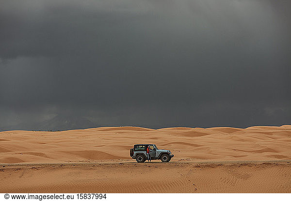 woman and her jeep while driving across sand dunes under stormy skies