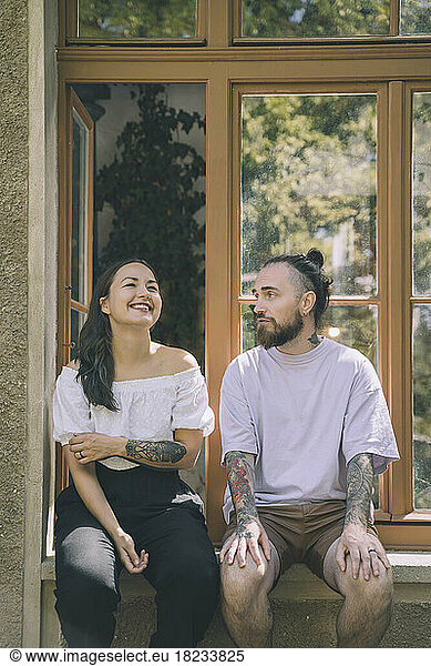 Woman and hipster man sitting on window sill talking to each other