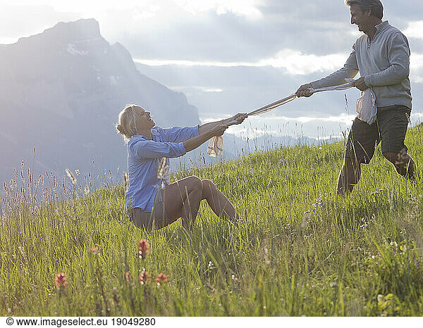 Woman and man play tug-o-war in mountain meadow