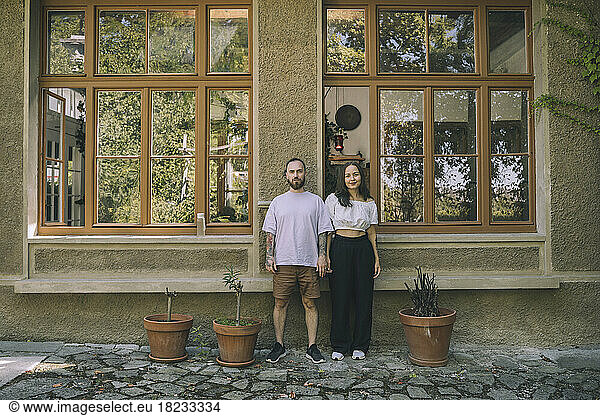 Woman and man standing amidst potted plants in front of window