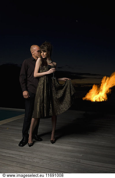Woman and man standing beside a swimming pool  flames in the background.