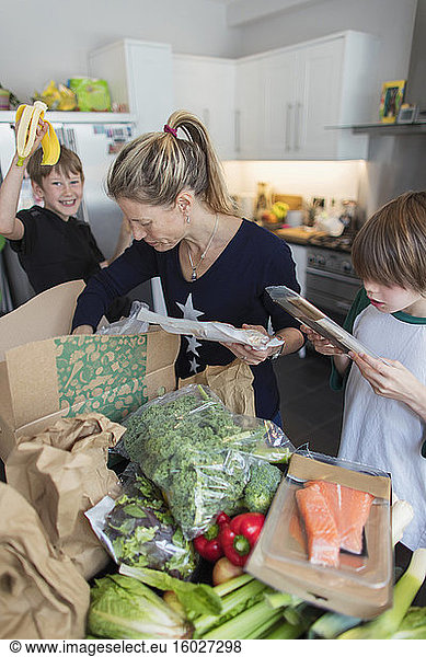 Woman and sons unloading fresh produce from box in kitchen