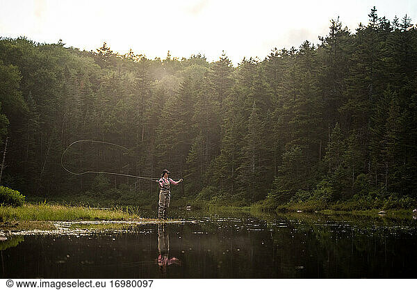Woman angler fly-fishing in NH backcountry lake during afternoon light