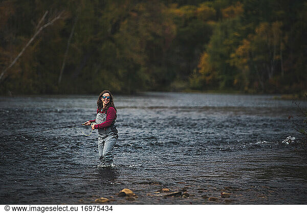 Woman angler walking through water with fly rod and foliage