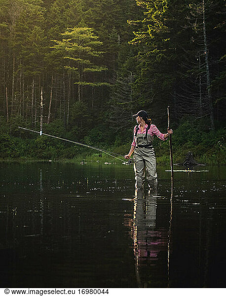Woman angler with fly rod and wading stick in NH backcountry lake