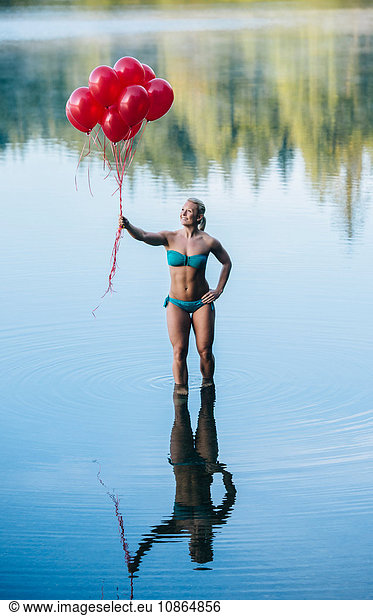 Woman ankle deep in water holding bunch of red balloons
