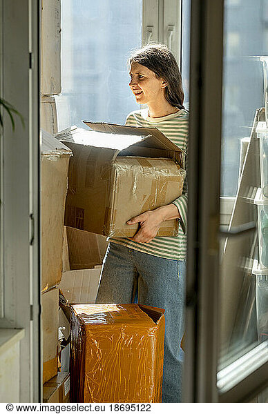 Woman arranging cardboard boxes by window at home