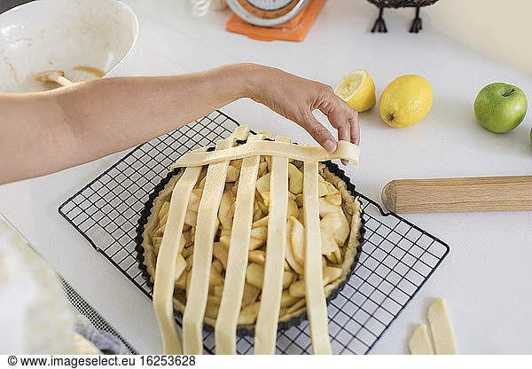 Woman arranging lattice over apple pie in kitchen