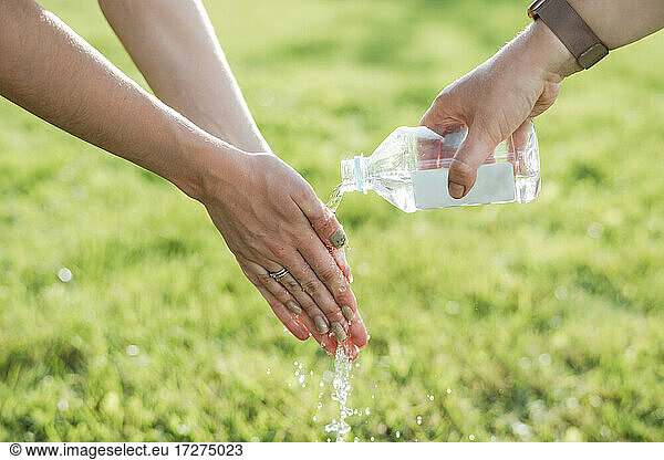 Woman assisting friend in washing hands from water at park on sunny day