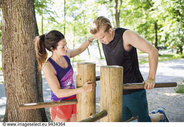 Woman assisting man in doing chin-ups on wooden bars at outdoor health club