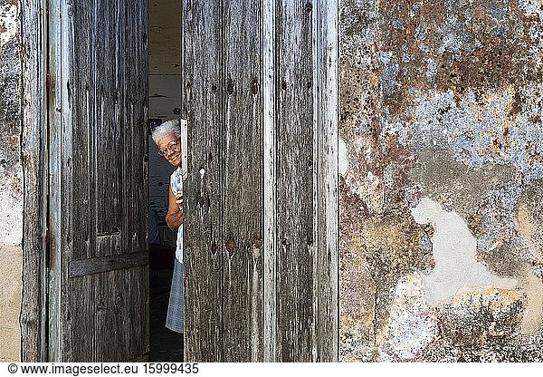 Woman at the entrance of her house with a decayed fa?ade of crumbling plaster and a weathered wooden door. Gibara  Cuba.