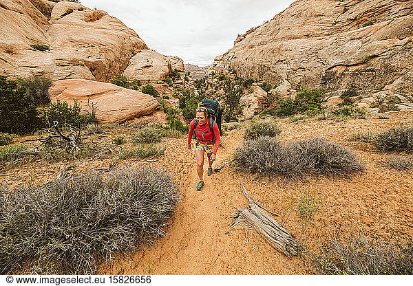 woman backpacks through sand under sandstone canyons of canyonlands