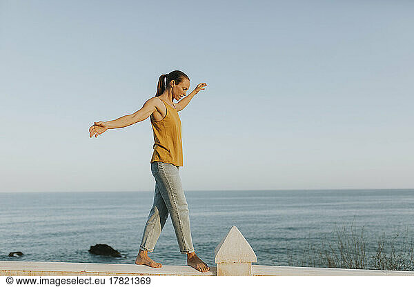 Woman balancing on railing at the sea on sunny day