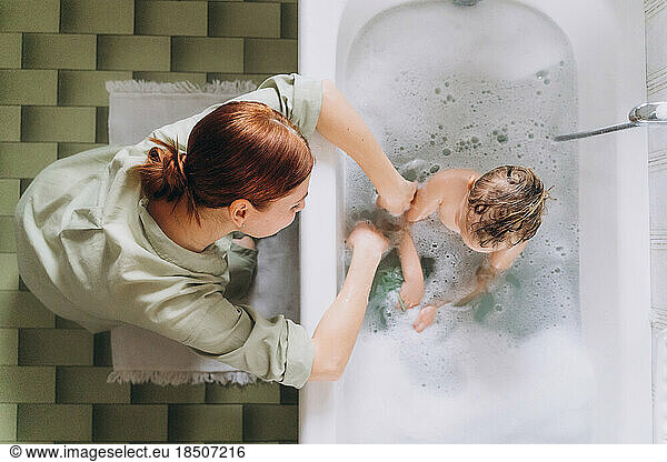Woman bathes a little happy girl in the bathroom with foam