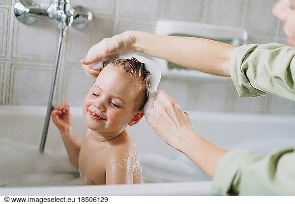 Woman bathes a little happy girl  Shampooing her hair