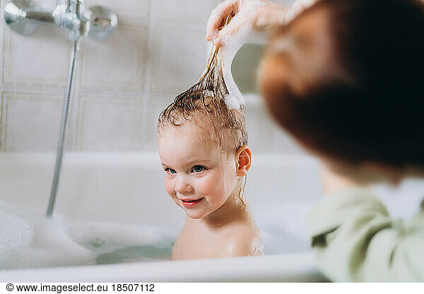 Woman bathes a little happy girl  Shampooing her hair