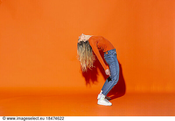 Woman bending over backwards against orange background