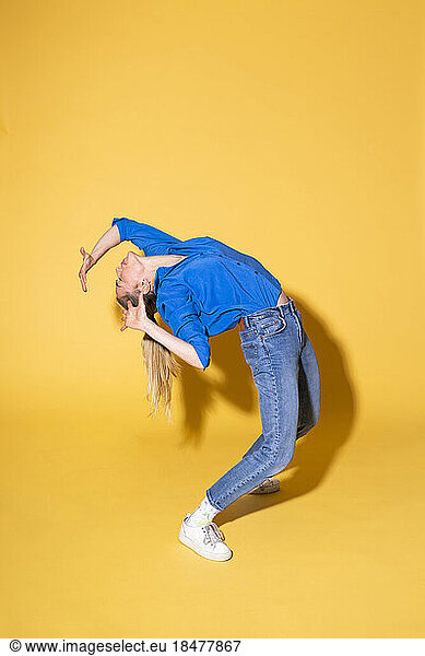 Woman bending over backwards against yellow background