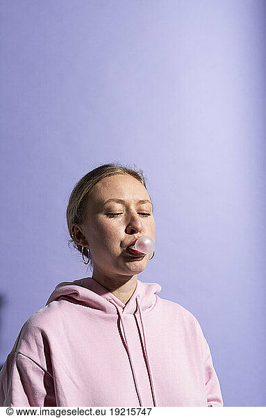 Woman blowing bubble gum against purple background