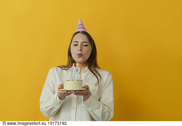 Woman blowing candle on birthday cake against yellow background