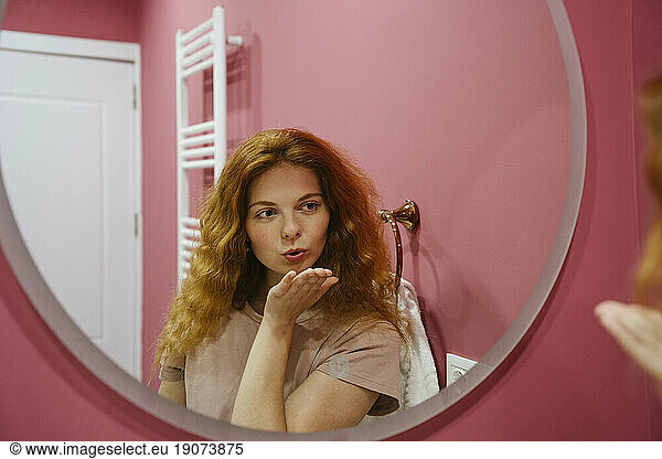 Woman blowing kiss looking in mirror at home